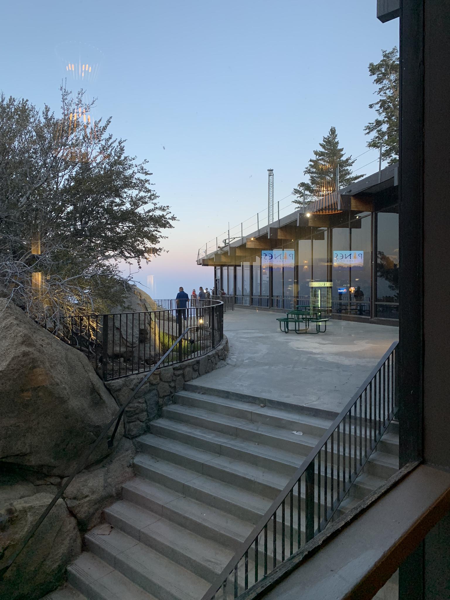People on an outdoor viewing deck at dusk, overlooking a vast landscape.
