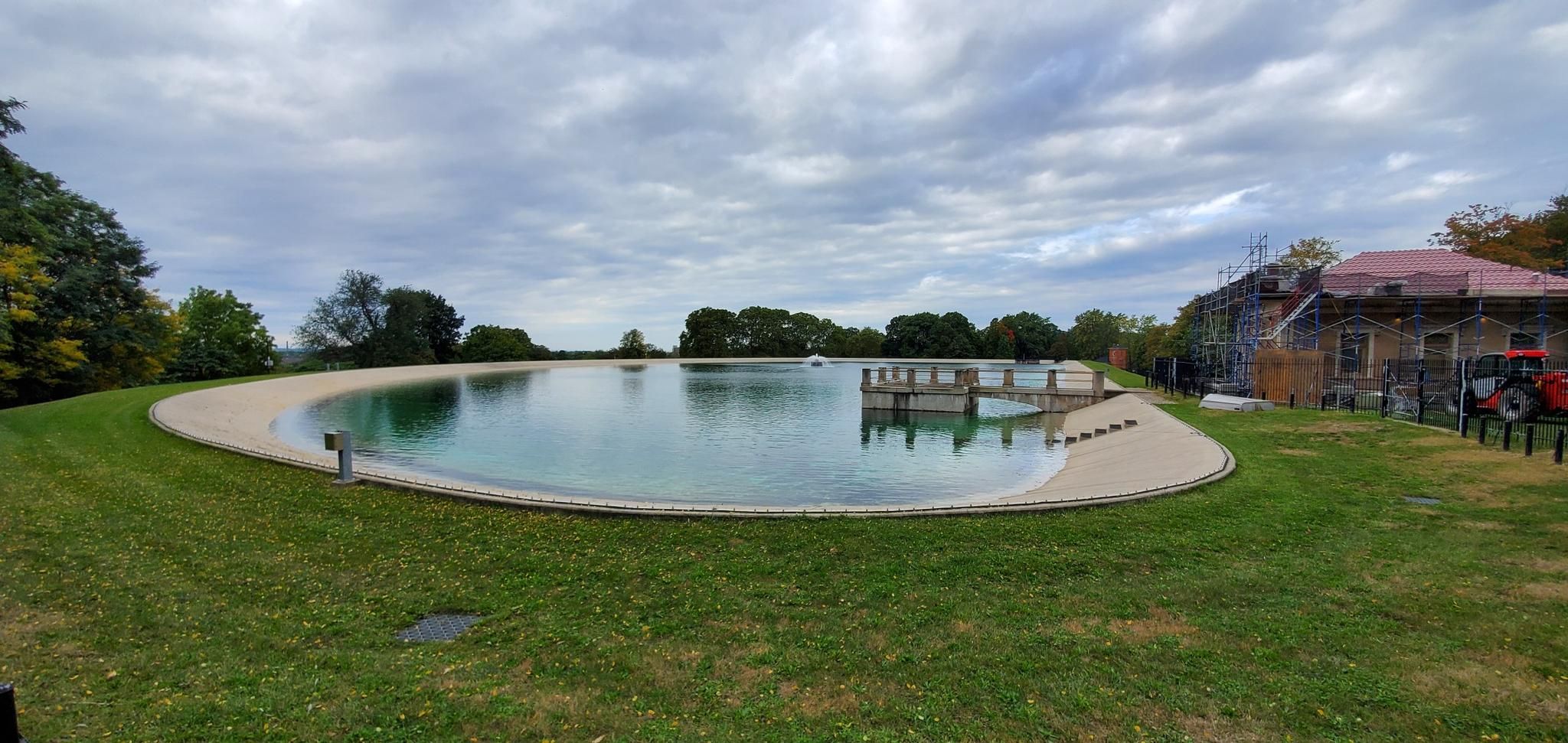 Large, oval reservoir with clear water, surrounded by green grass under cloudy sky. - Highland Reservoir Loop Trail