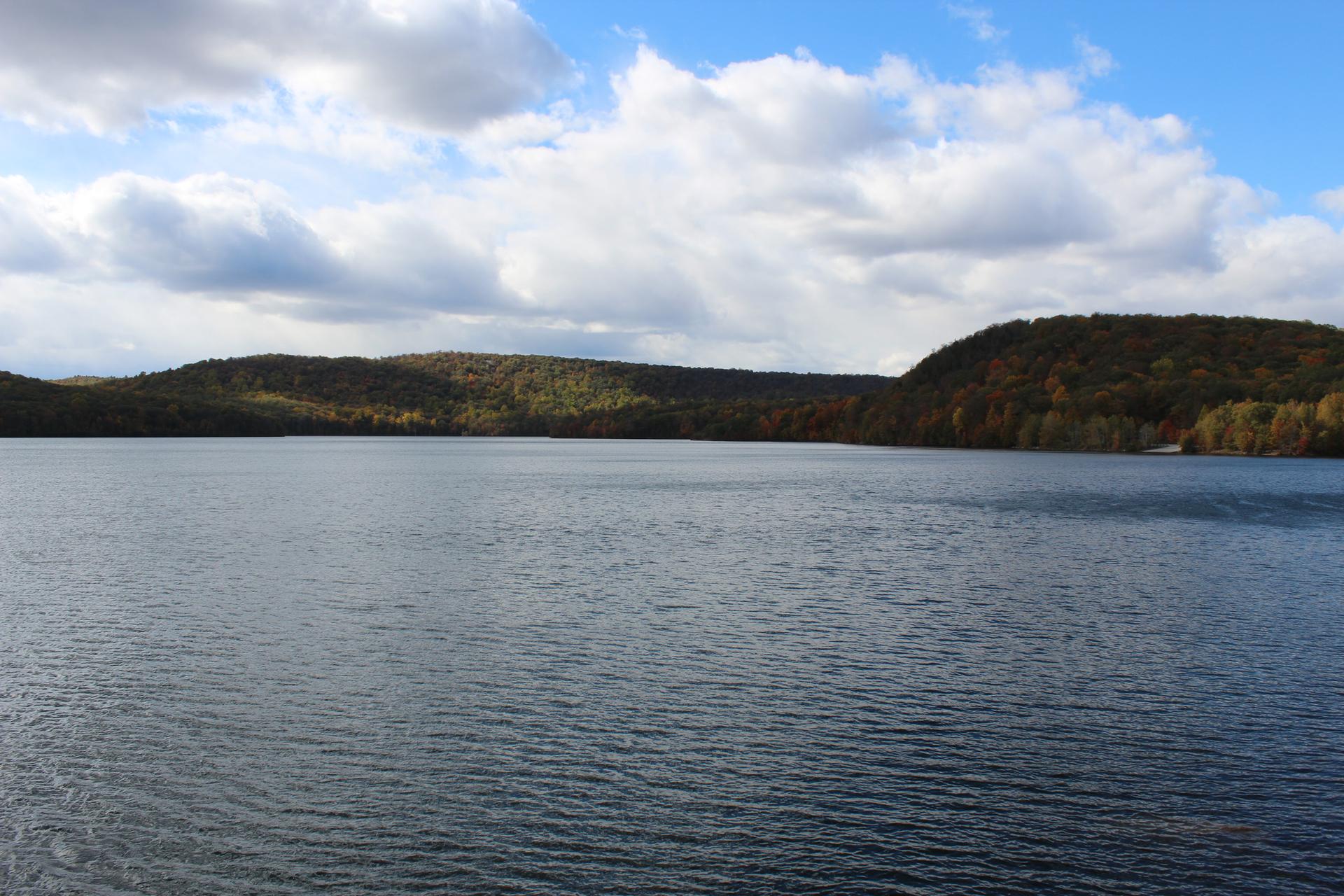 Wide lake with forested hills under a partly cloudy sky.