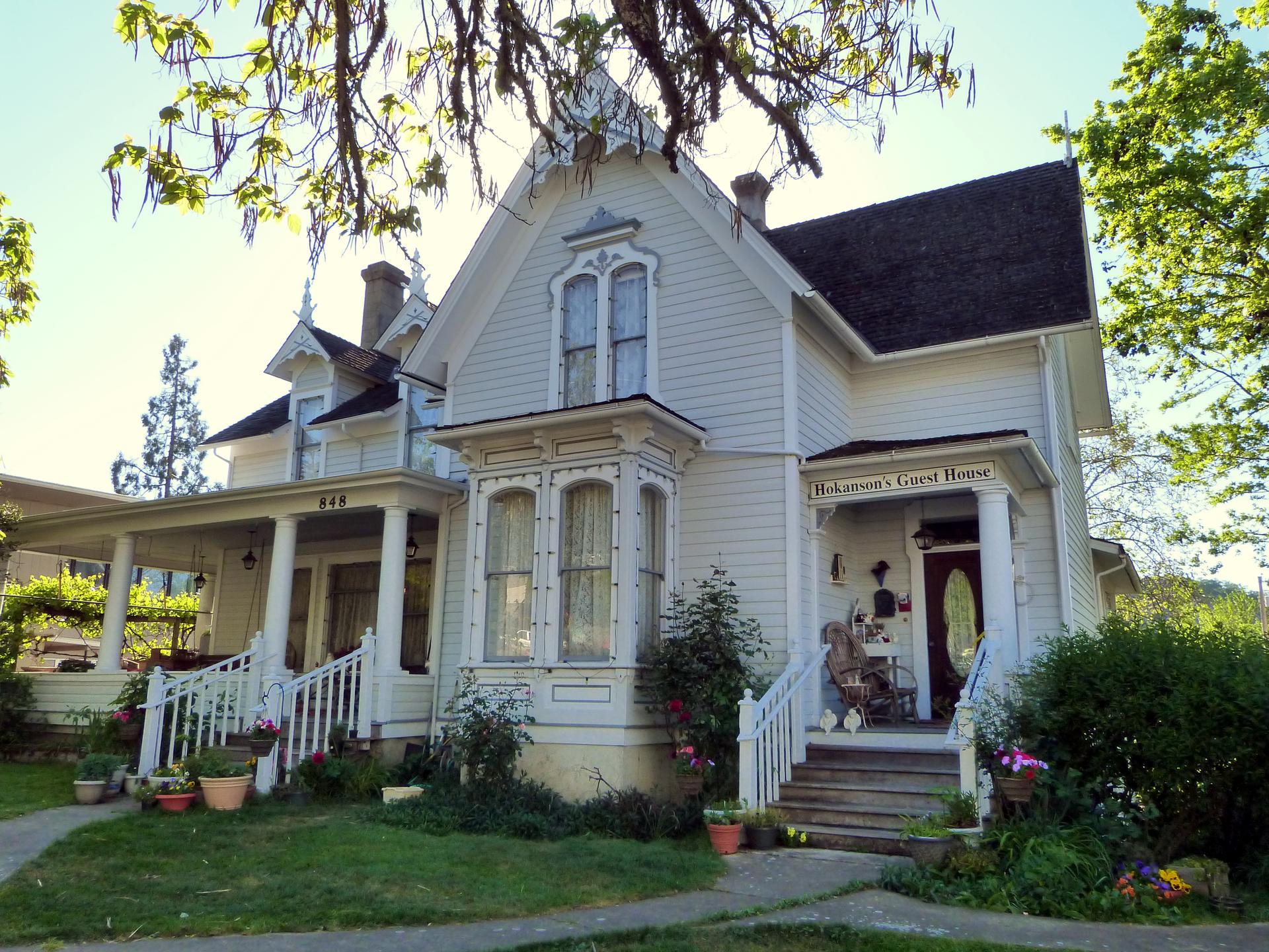 Ornate white Victorian house with a porch and green lawn on a sunny day.