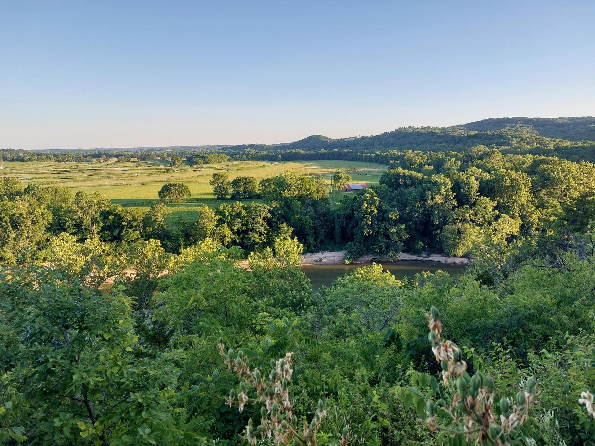 Expansive green landscape with a river winding through dense trees under clear skies.