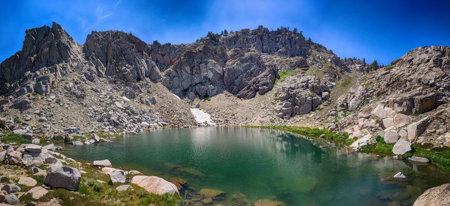Clear green alpine lake surrounded by rugged, rocky mountains under blue sky.