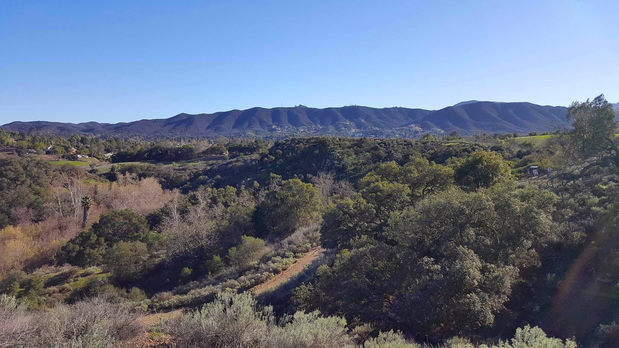 Expansive view of green hills and distant mountains under a clear blue sky. - Sundown Trail