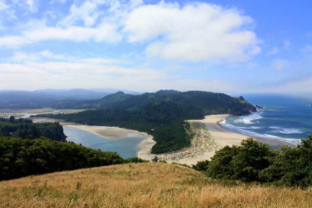 Panoramic view of a river estuary, sandy beach, and ocean under a cloudy sky.