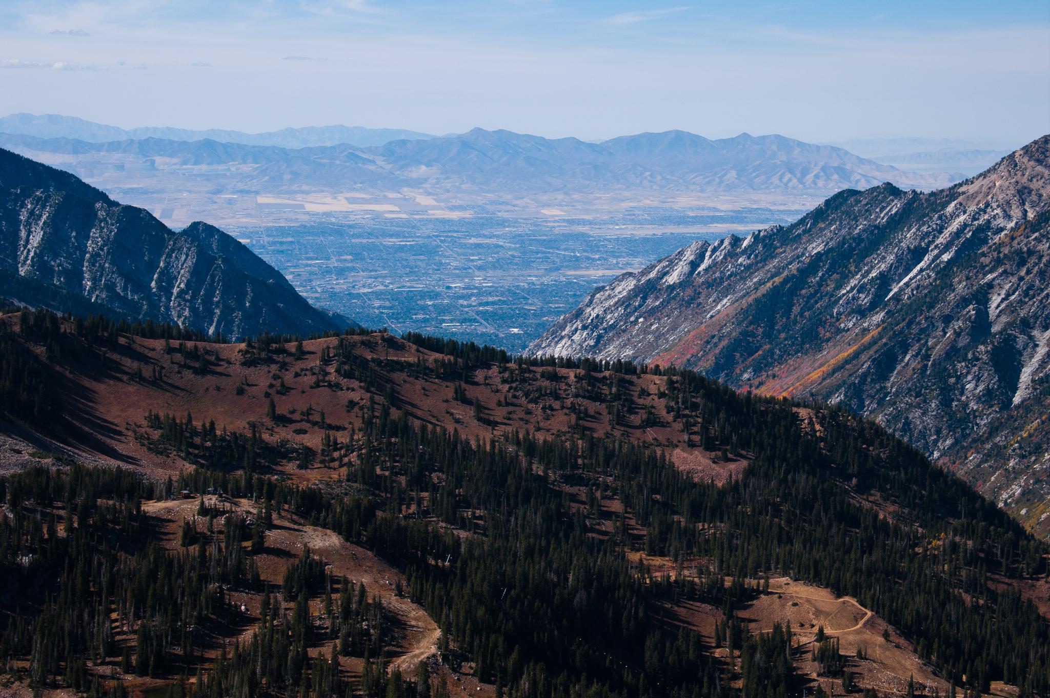 Panoramic view of rugged mountains, forested slopes, and a distant valley city.