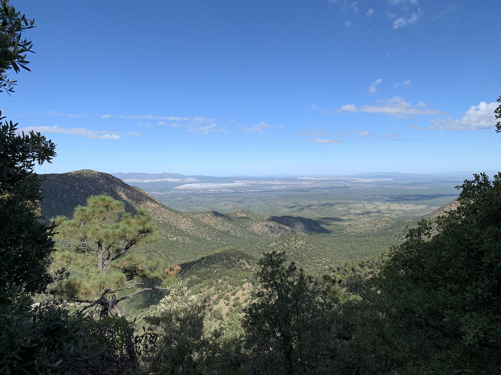 Expansive view of green mountains and distant plains under a clear blue sky.