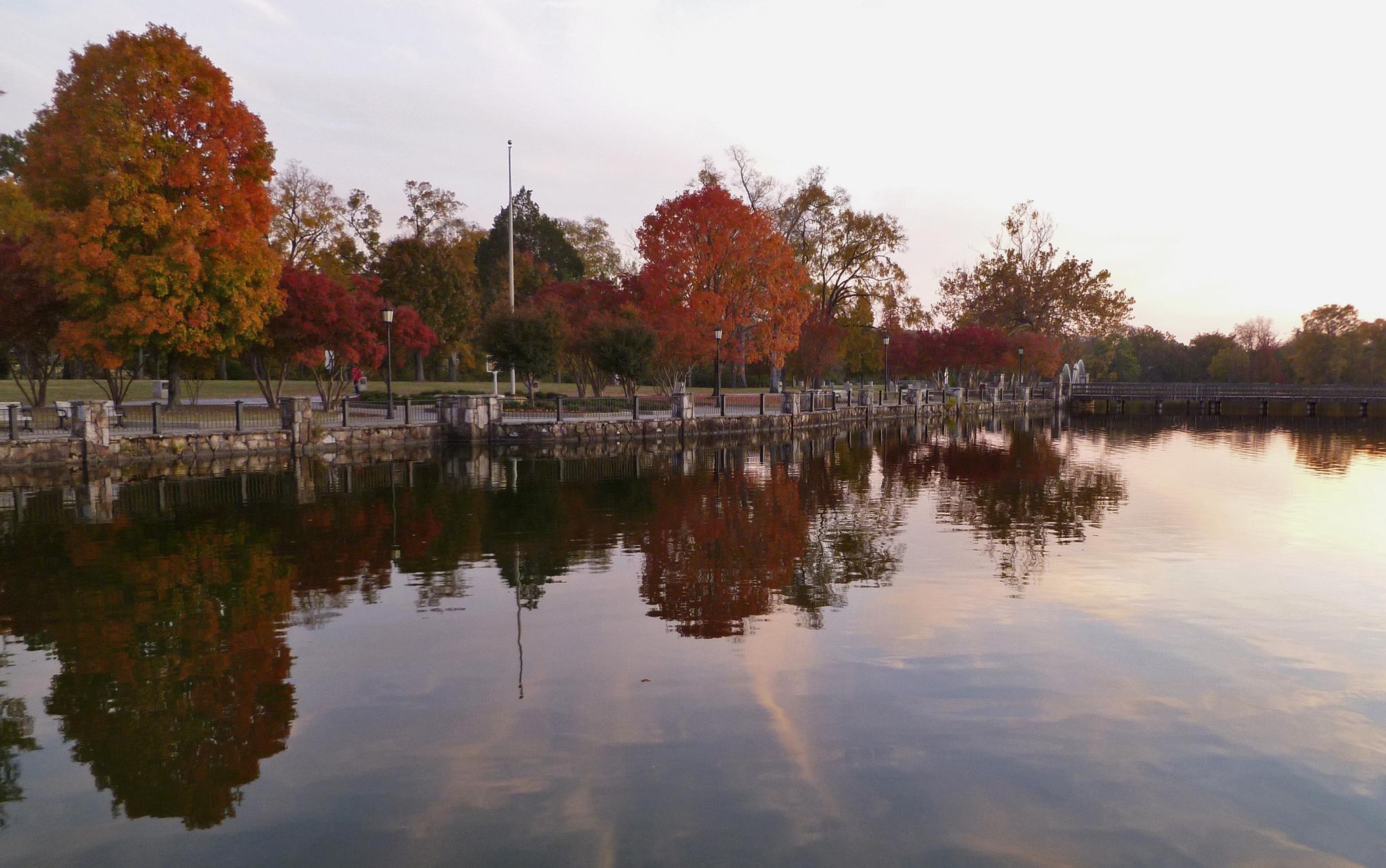Calm water reflects colorful autumn trees and a stone-lined shore under soft light.