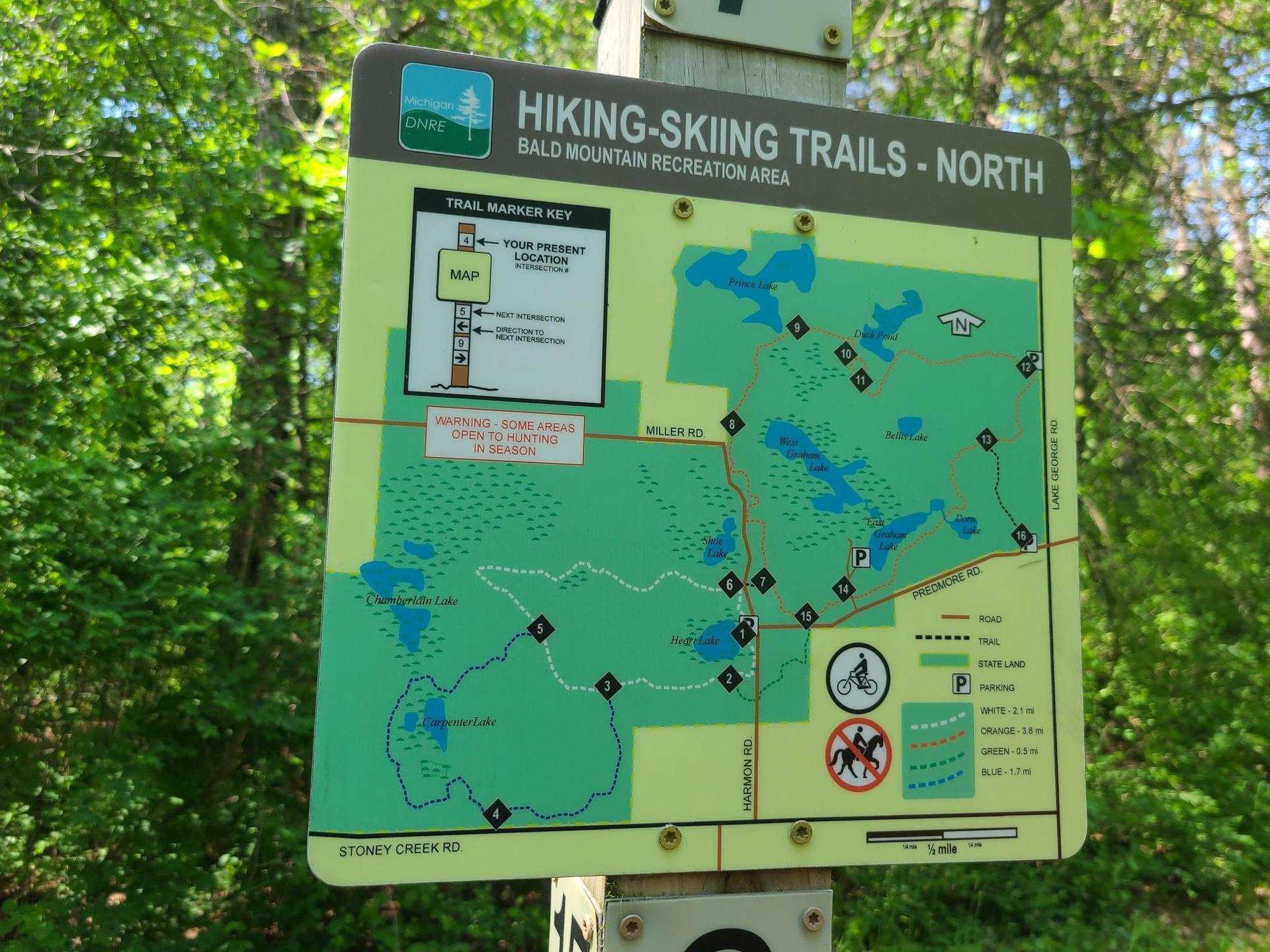 Close-up of a green hiking trail map sign in a wooded area.