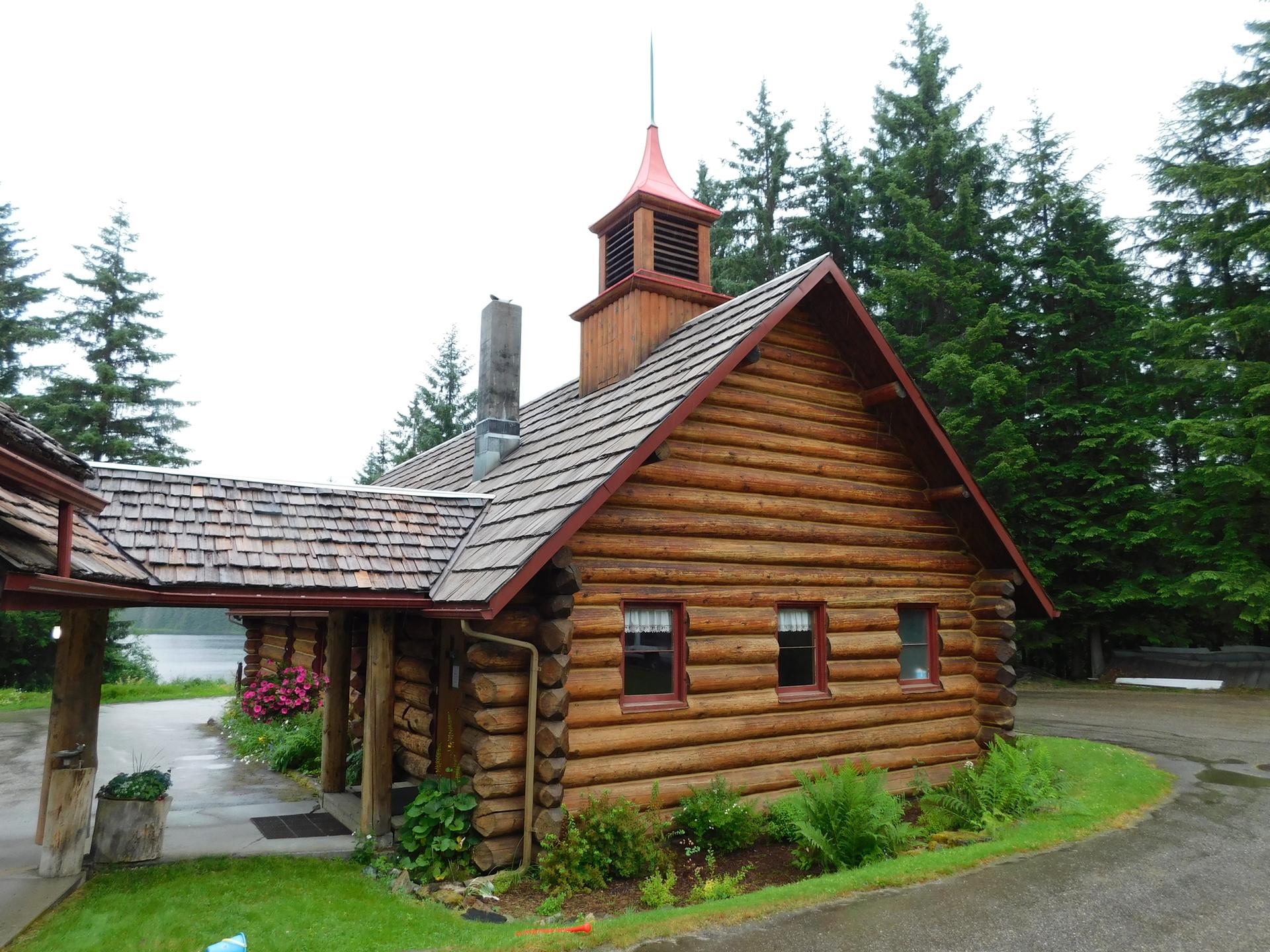 Rustic log cabin with a red steeple surrounded by tall evergreen trees.
