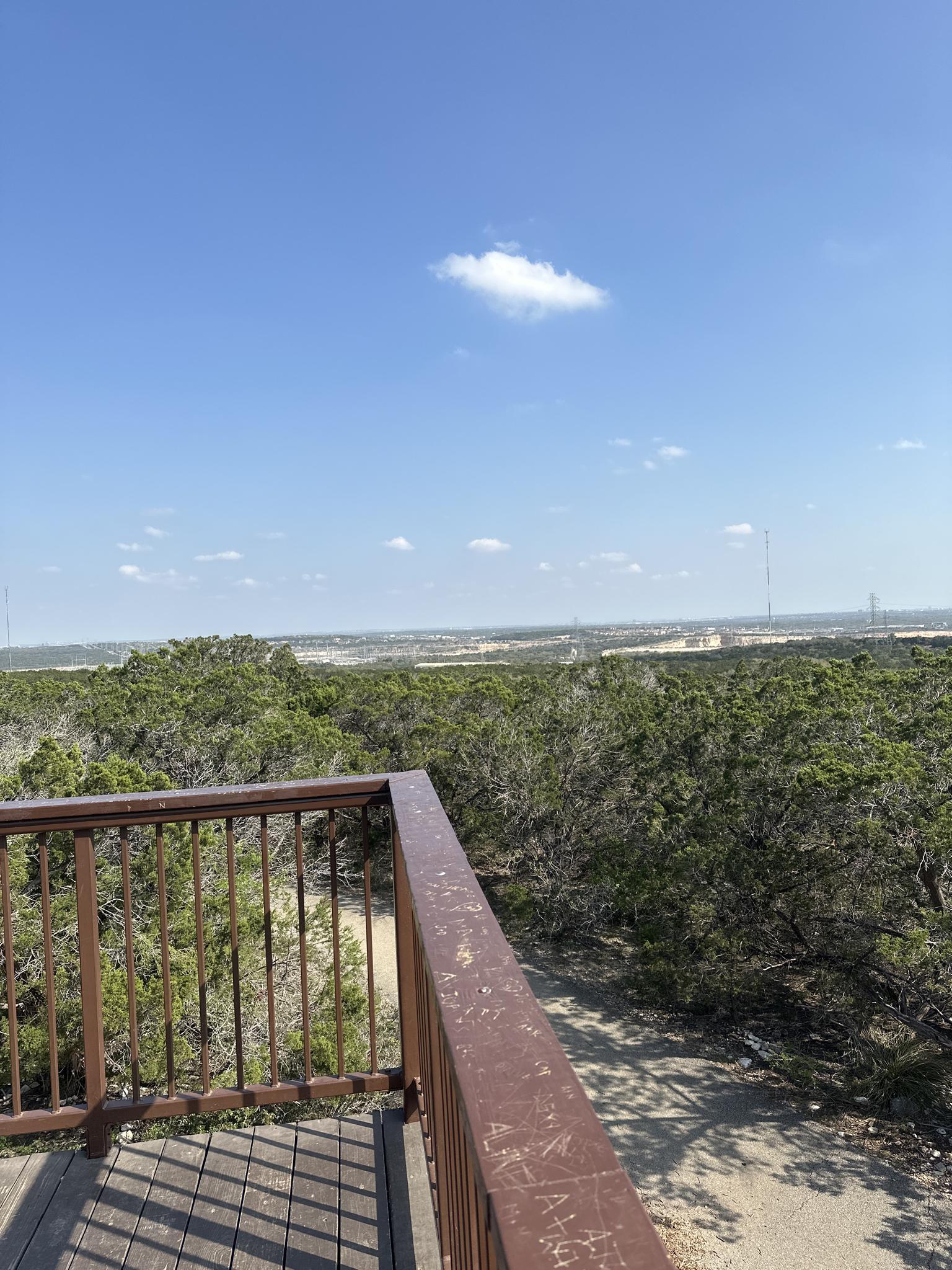An observation deck overlooks a vast green landscape under a blue sky.