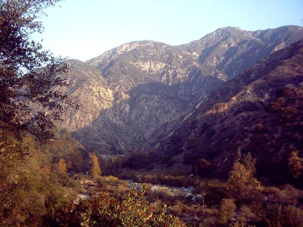 A deep, rocky mountain canyon with a dry riverbed and autumn trees.