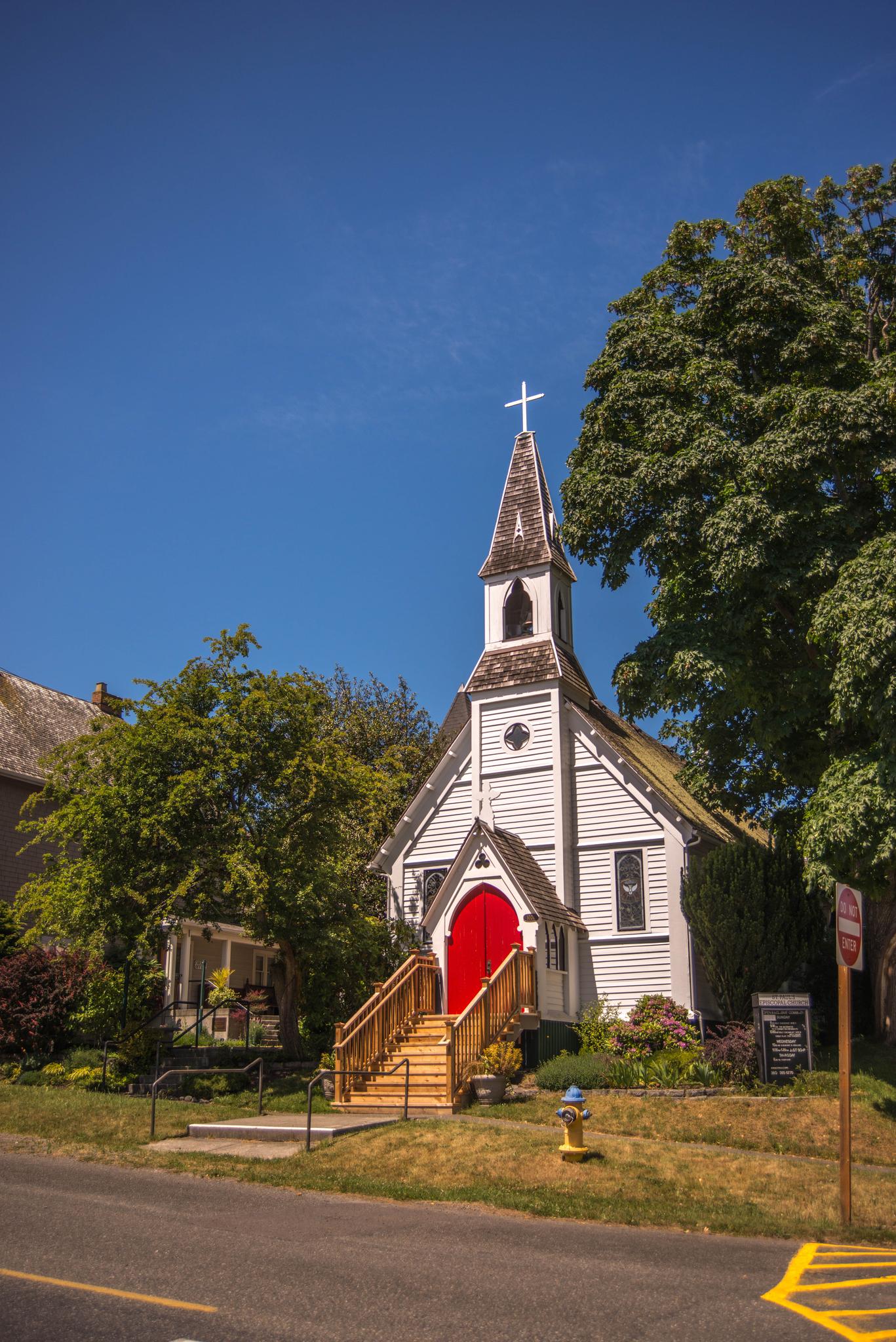 A white church with a steeple and red doors under a clear blue sky.