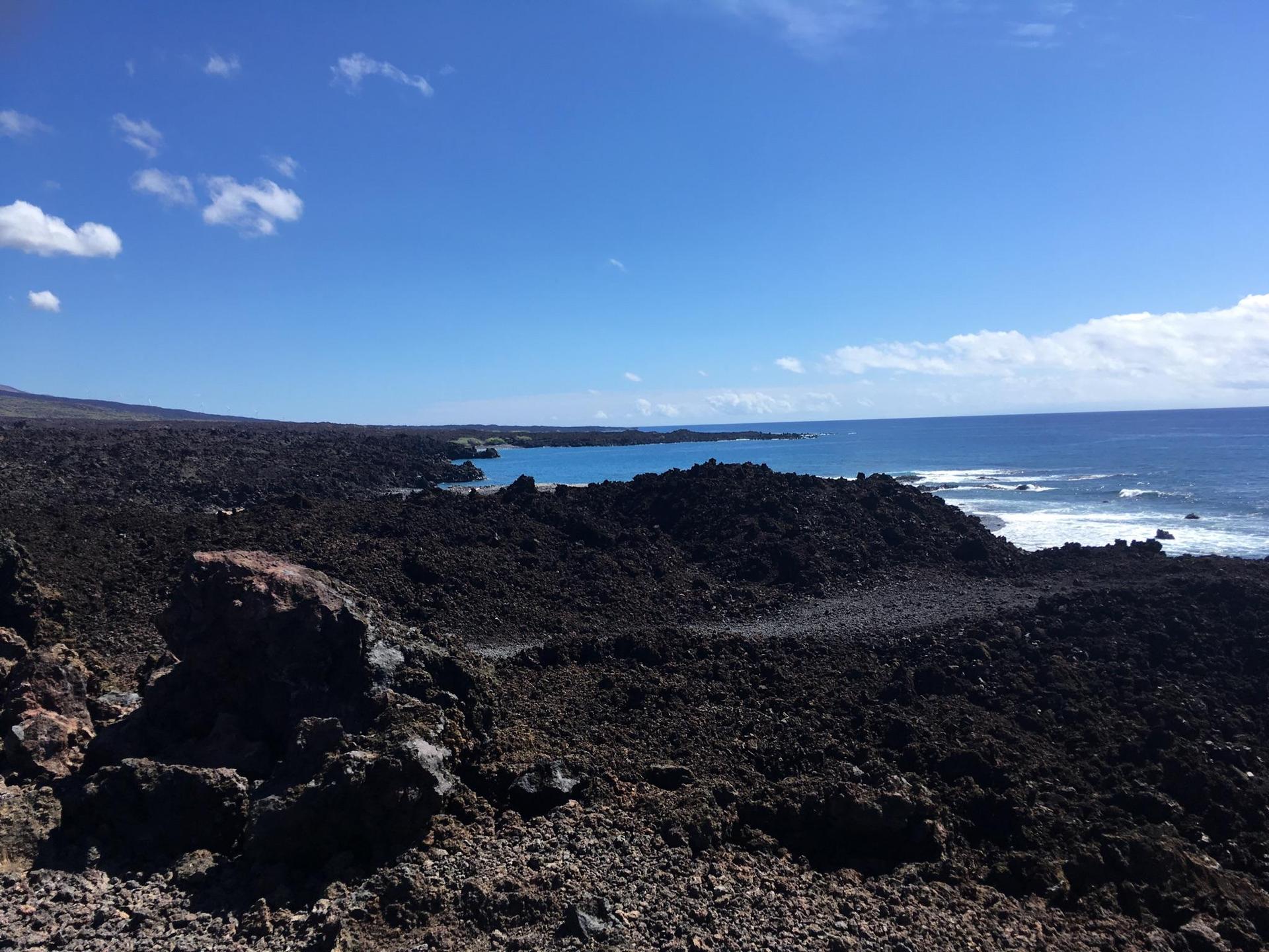 Vast, sunny landscape of dark lava fields meeting a blue ocean.