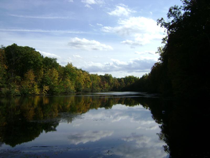 Calm water reflecting cloudy sky and colorful autumn trees on the banks.