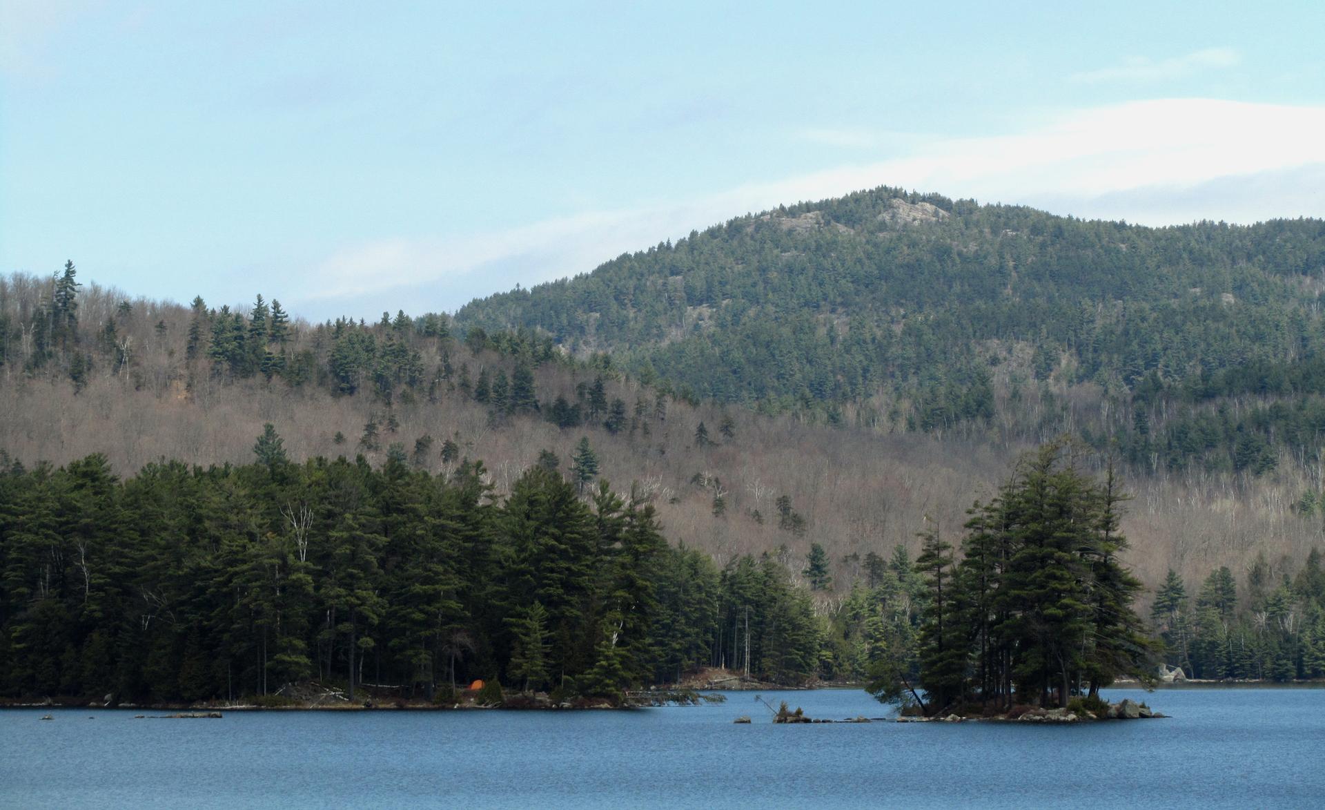 A blue lake with forested mountains, small islands, and a tiny orange tent.