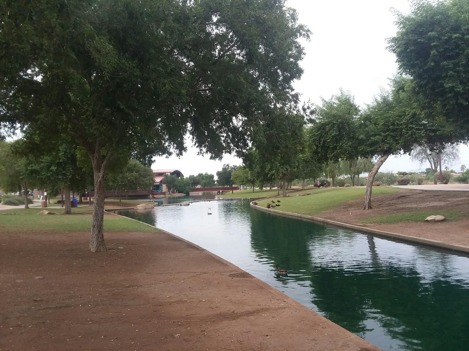 Serene canal bordered by green trees and grass under an overcast sky.