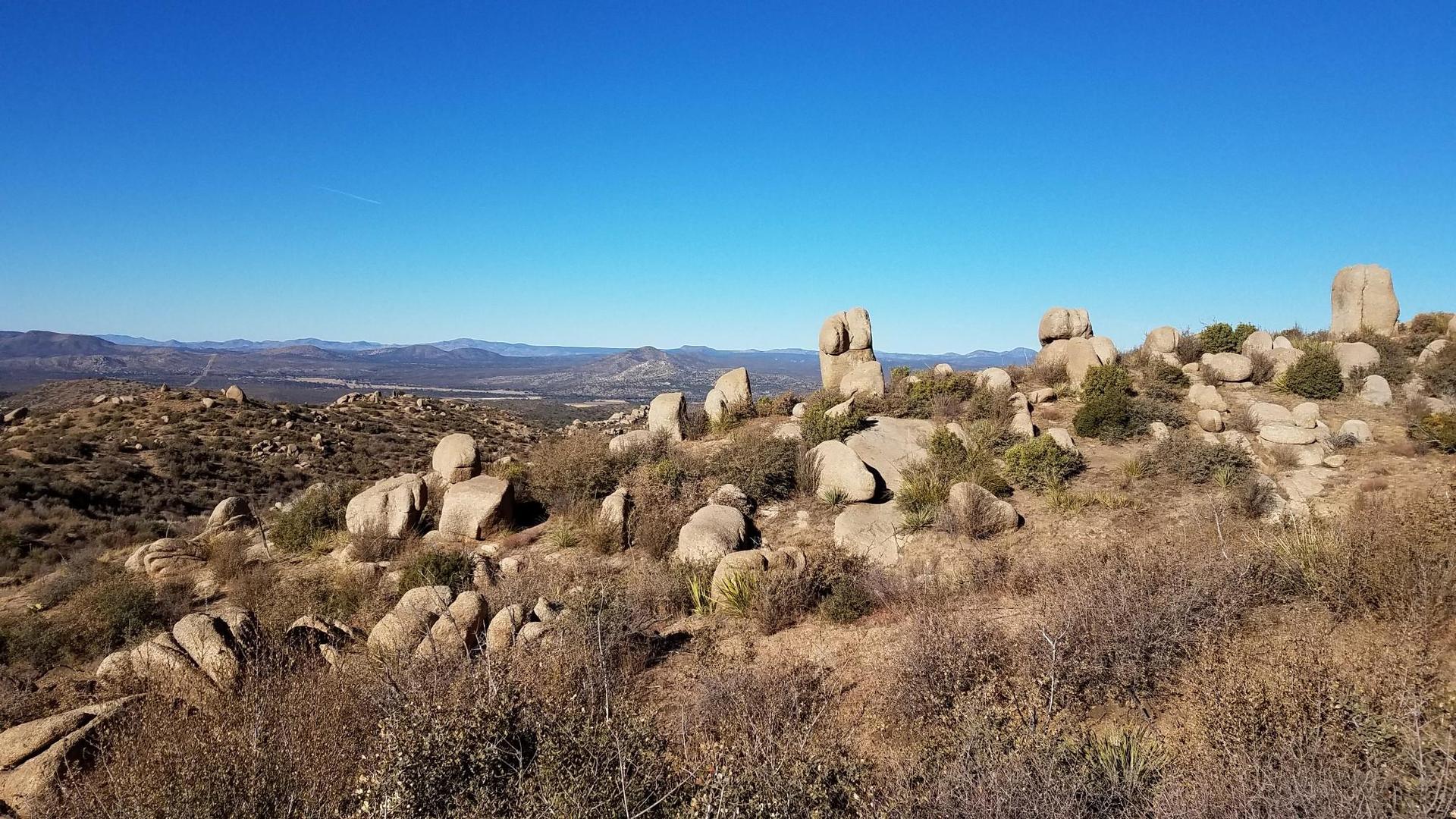 Arid landscape with large boulders and dry brush under a clear blue sky.