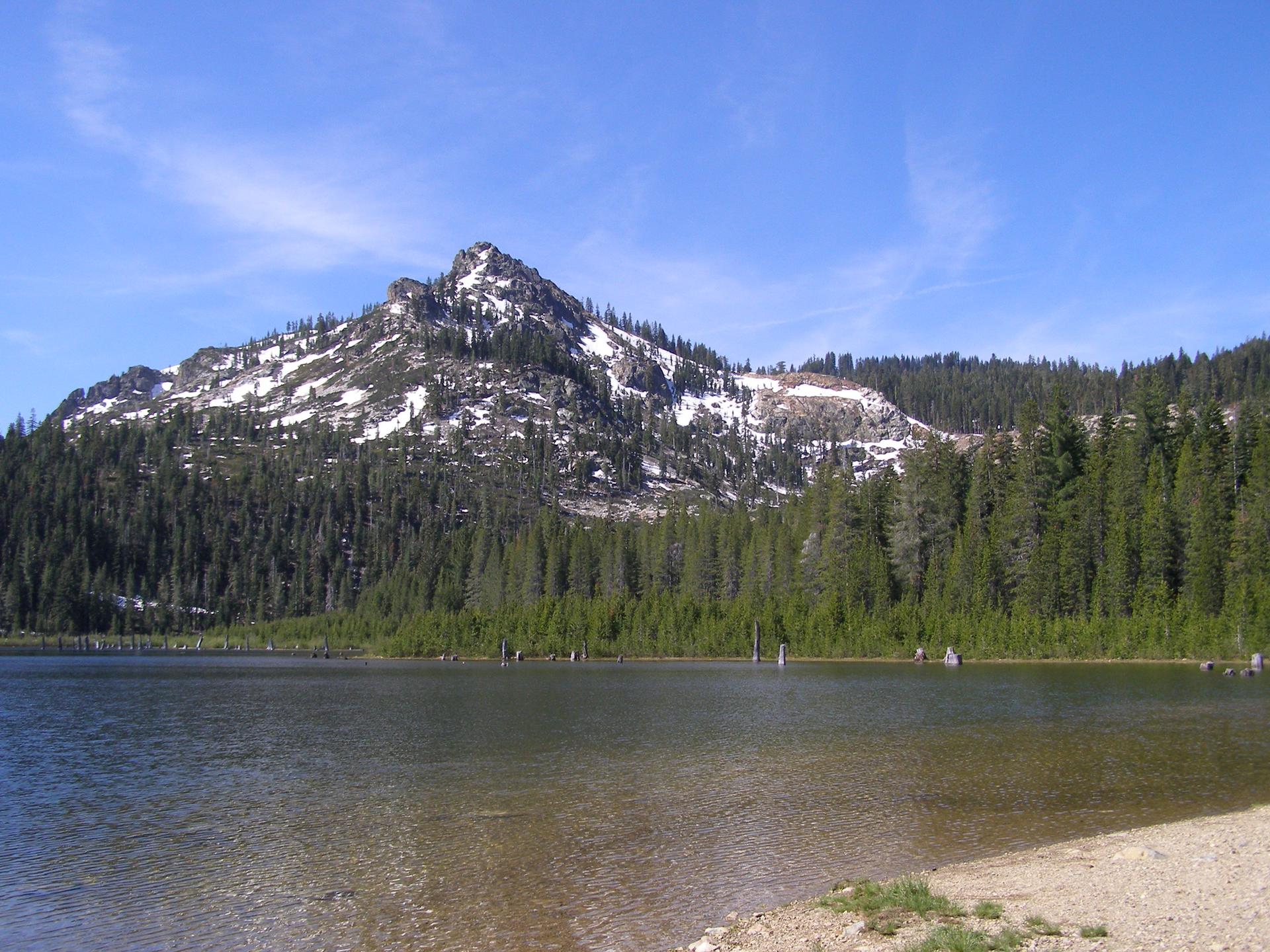 Calm lake reflecting a snow-dusted mountain and dense pine forest.