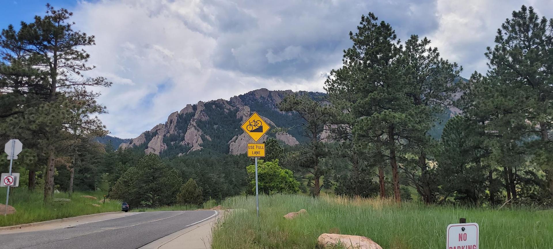 A road leads towards rocky mountains under cloudy sky, with a steep grade sign.