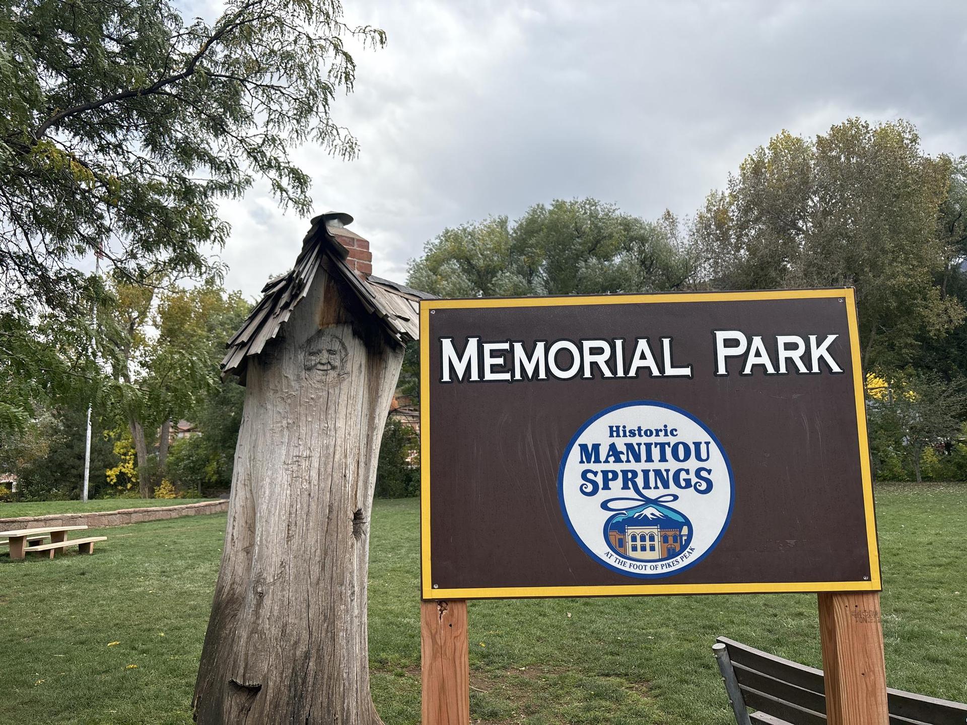 Park sign for "Memorial Park" beside a carved tree trunk on a cloudy day.