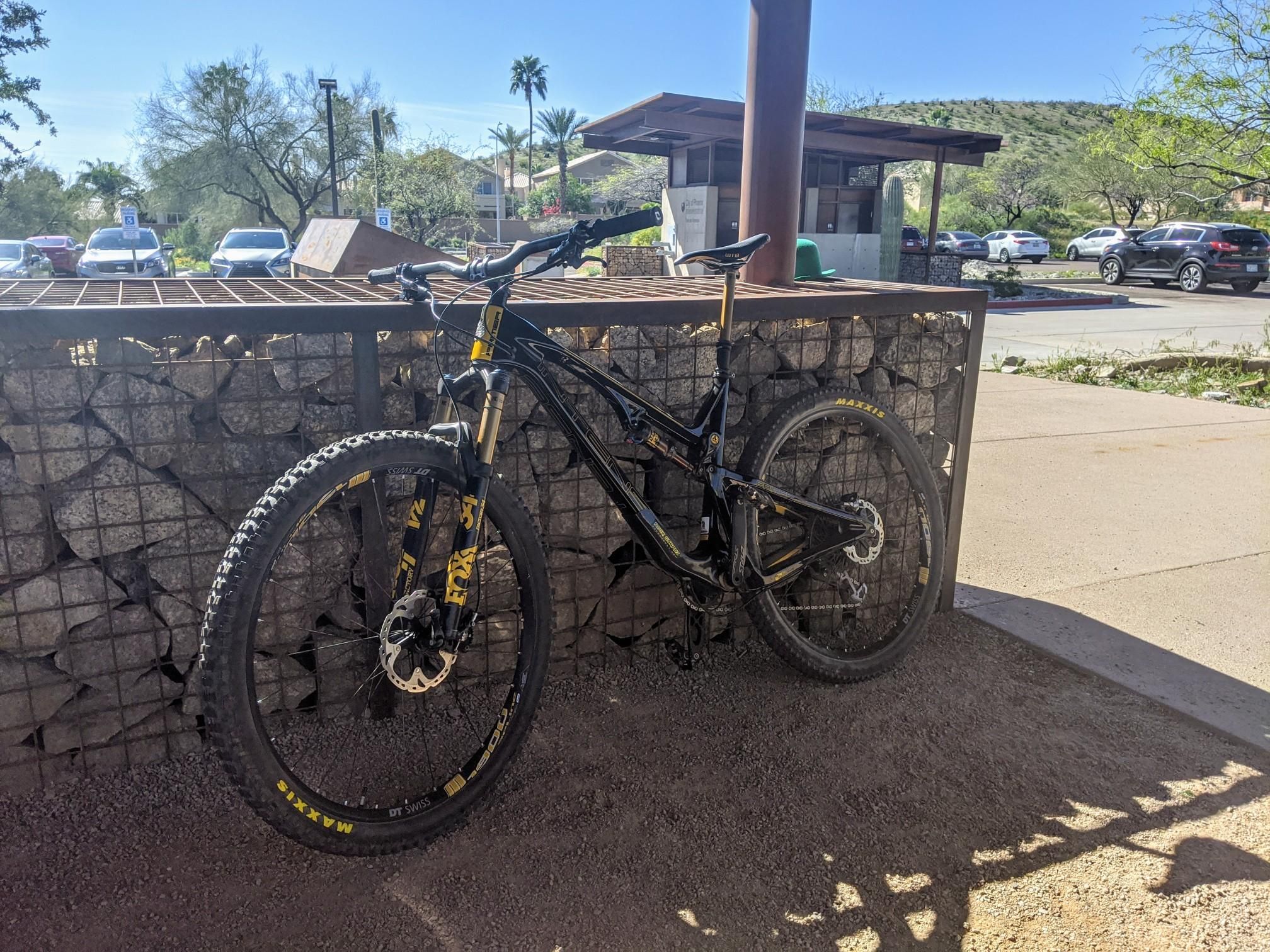 Black mountain bike parked next to a stone wall on a bright, sunny day. - Ahwatukee Foothills loop