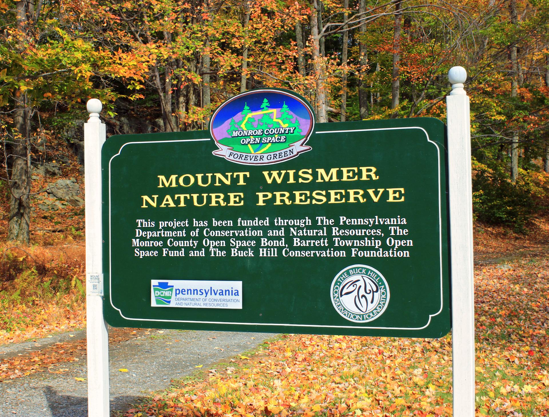 Green nature preserve sign on a sunny day with autumn trees.