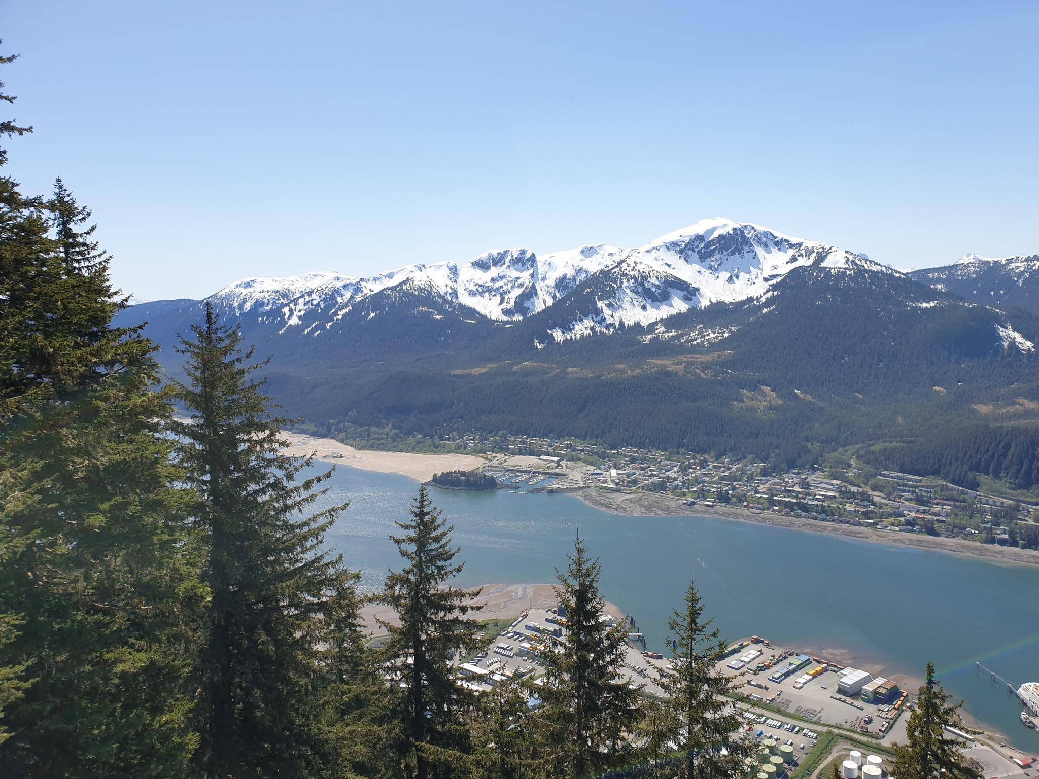 Panoramic view of a town by a bay, with snow-capped mountains and clear sky.