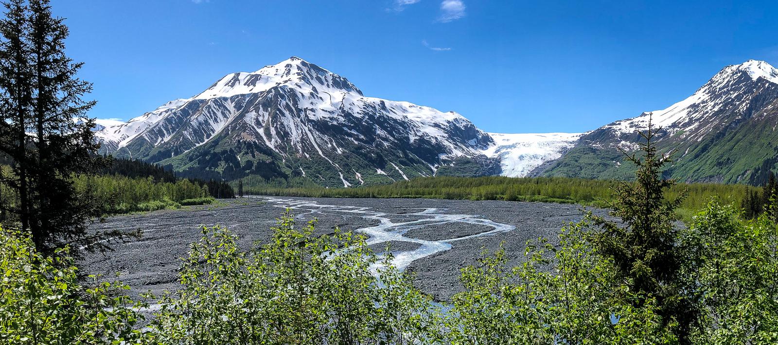 Panoramic view of snow-capped mountains, a glacier, and a braided river.