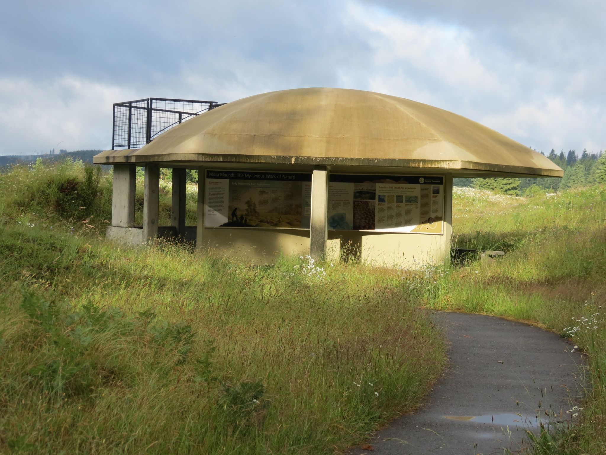 A concrete, mushroom-shaped building with an observation deck on a grassy hillside. - E-Line Road loop from Mima Mounds Natural Area Preserve