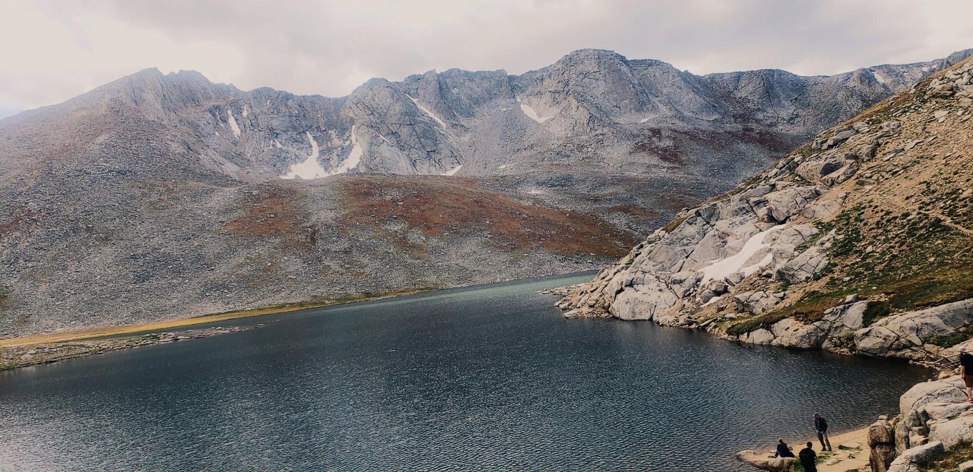 Mountain lake surrounded by rugged peaks and rocky shores, with people visible.