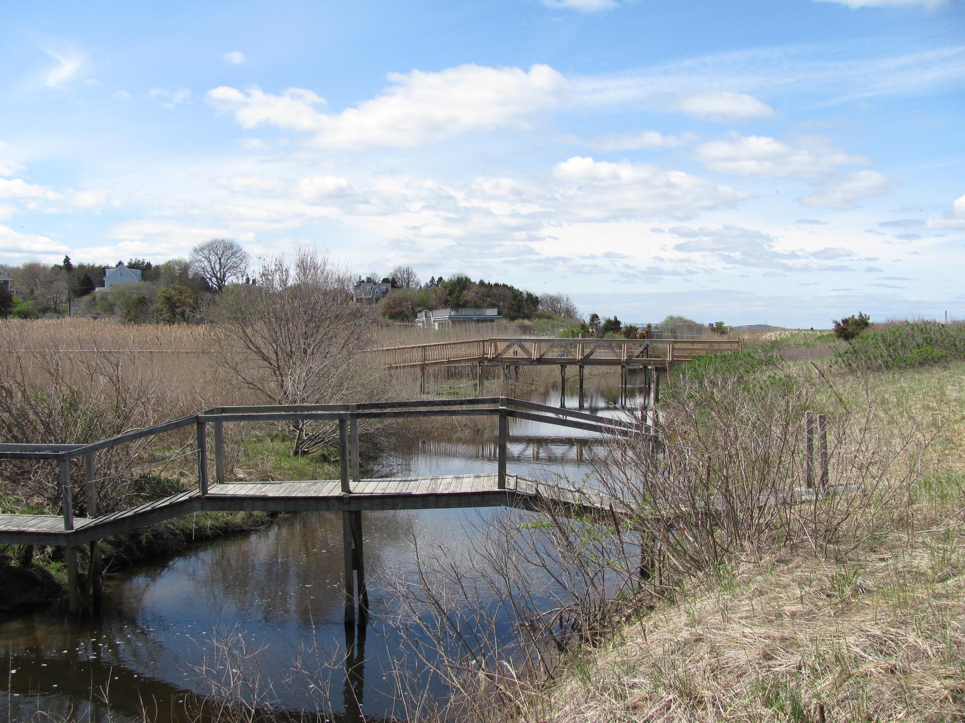 Wooden bridges cross a narrow waterway under a bright, cloudy sky.