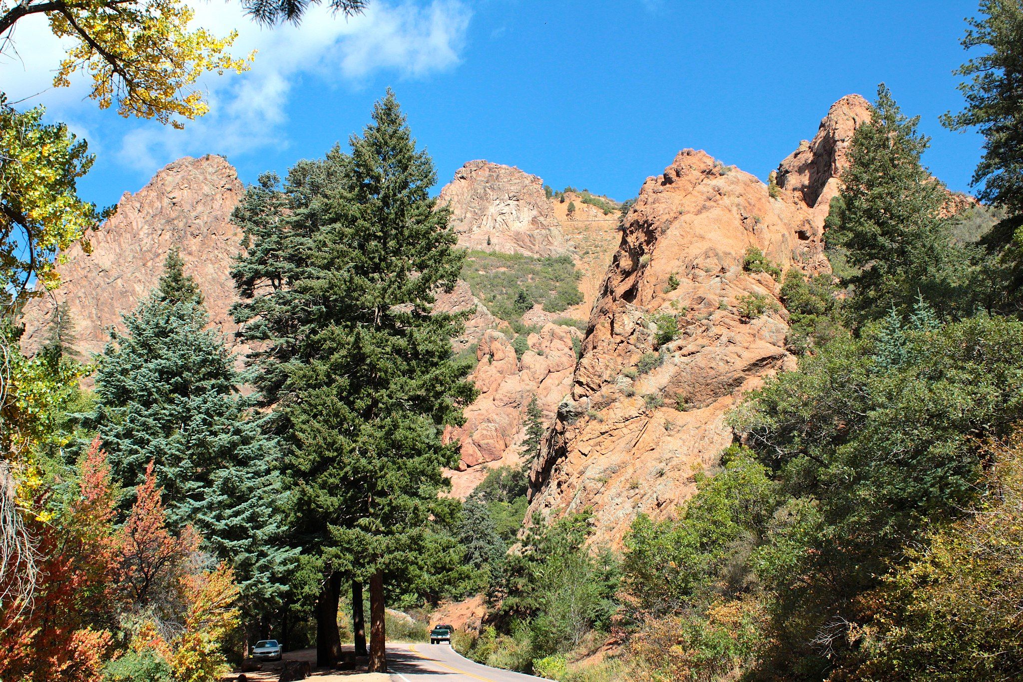 Sunny view of rugged mountains, evergreen trees, and a winding road. - Lower Columbine Trail loop from The Broadmoor