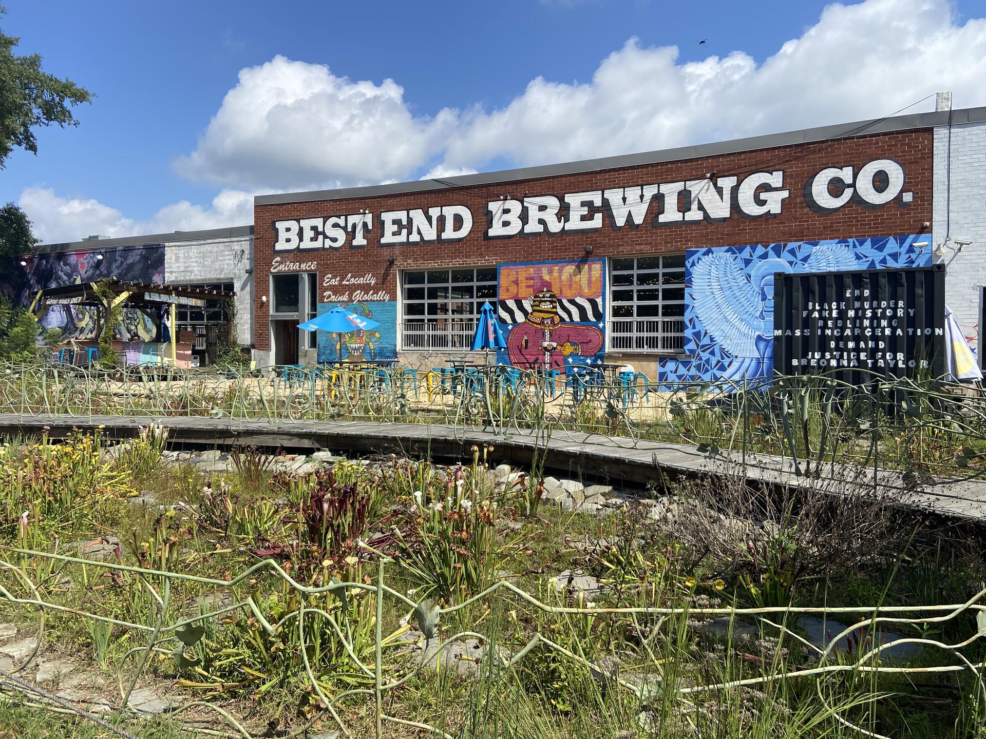 A brewery building with murals and an outdoor seating area under a blue sky.