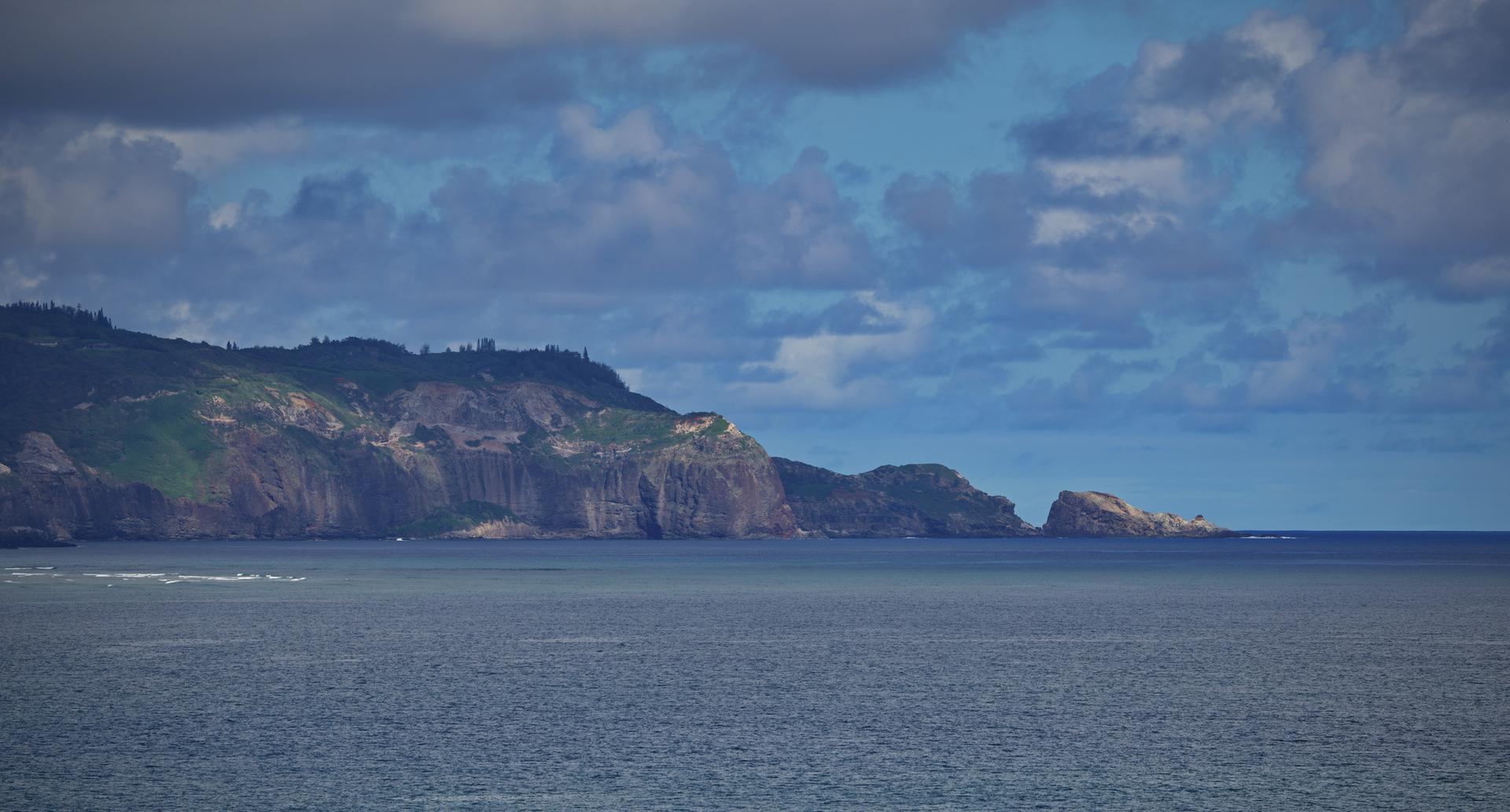Dramatic coastal cliffs meet the ocean under a cloudy, blue sky.