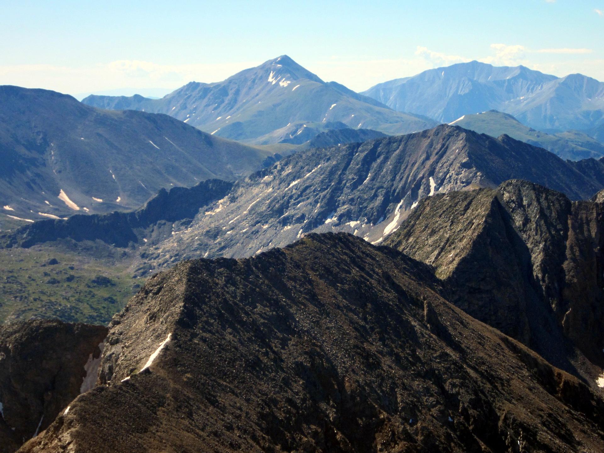 Panoramic view of rugged mountain peaks with snow patches under a clear sky.