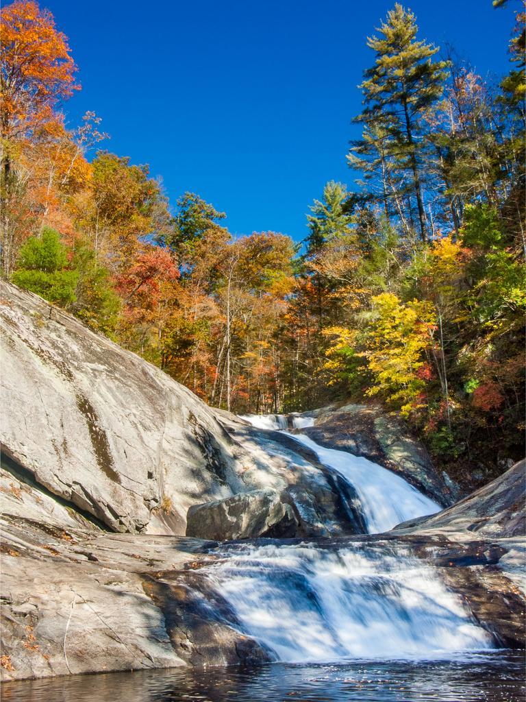 Waterfall cascades over rocks, surrounded by vibrant autumn trees under a clear blue sky.