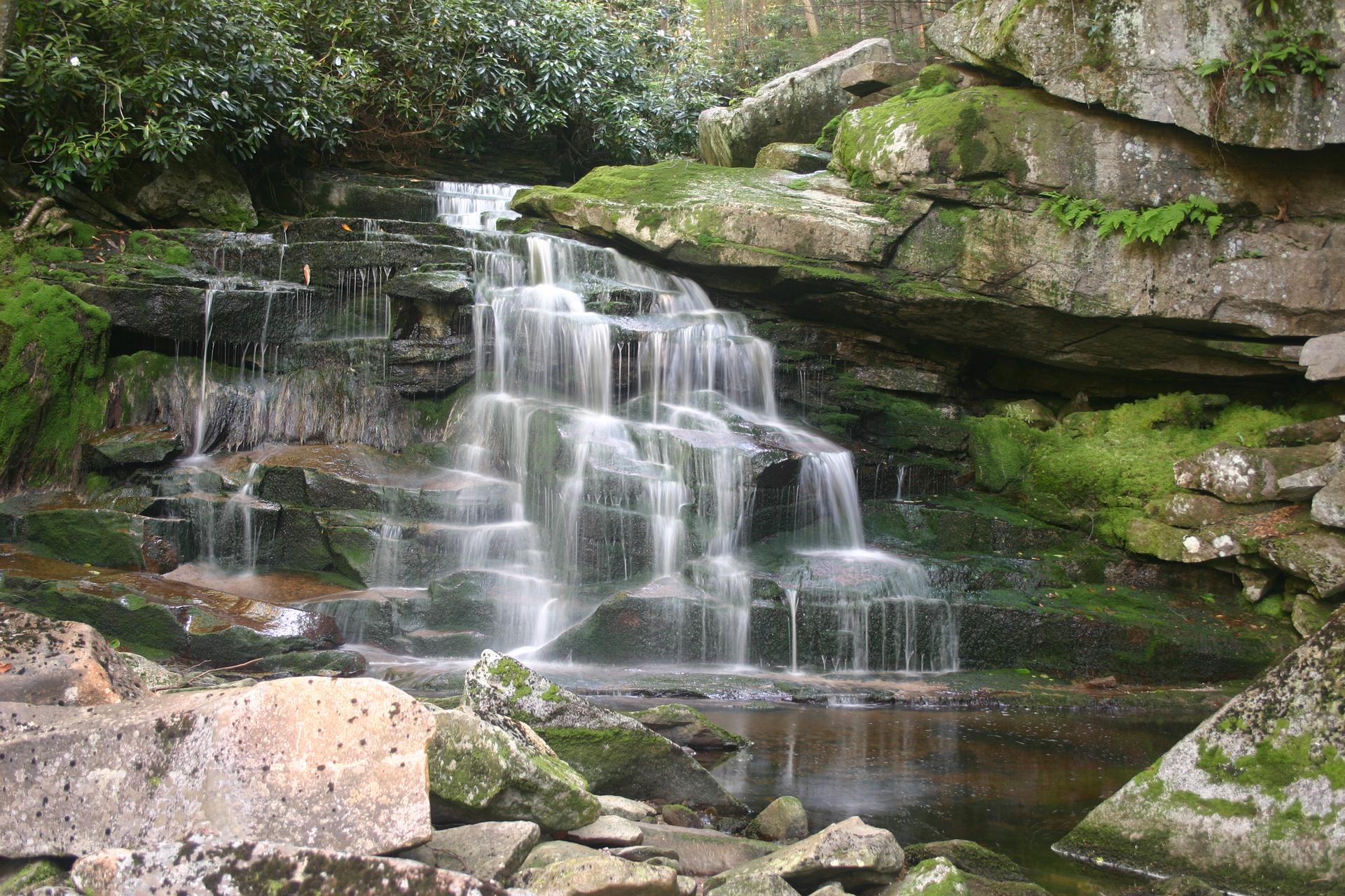 Beautiful tiered waterfall cascading over mossy rocks into a calm pool.