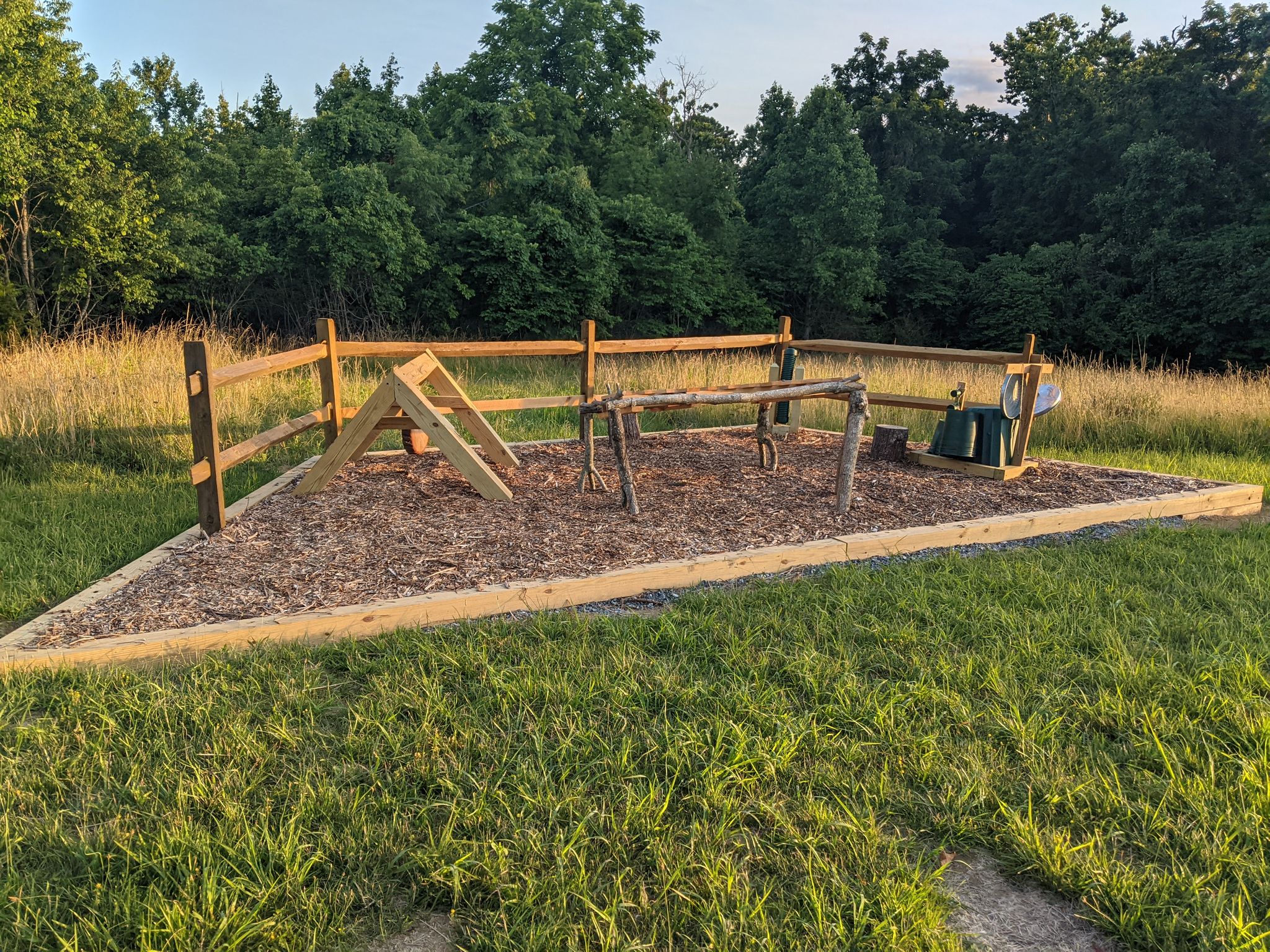 A fenced dog agility course in a grassy field with trees under bright light. - Skyline Trail