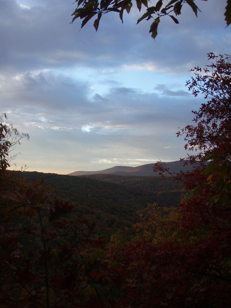 Overcast sky above a vast, forested mountain range at dusk.