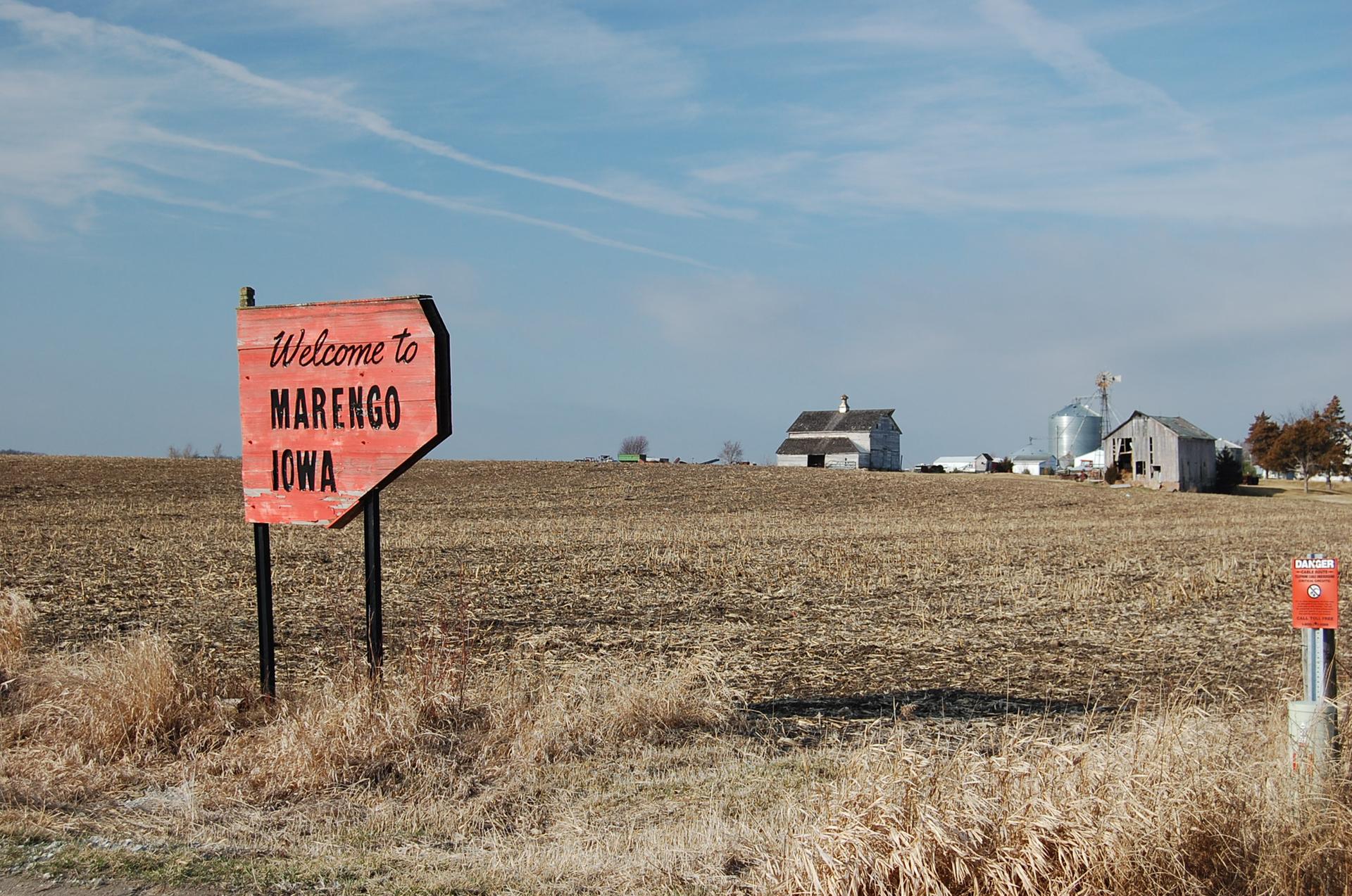 An orange directional sign in a dry, tilled field under a blue sky.