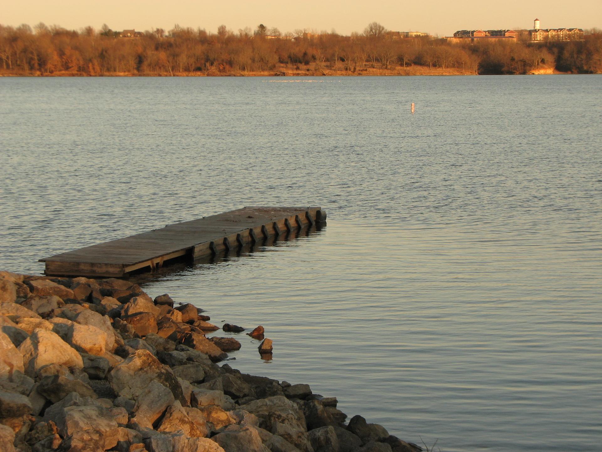 A wooden dock extends into calm water with a rocky shore at sunset.
