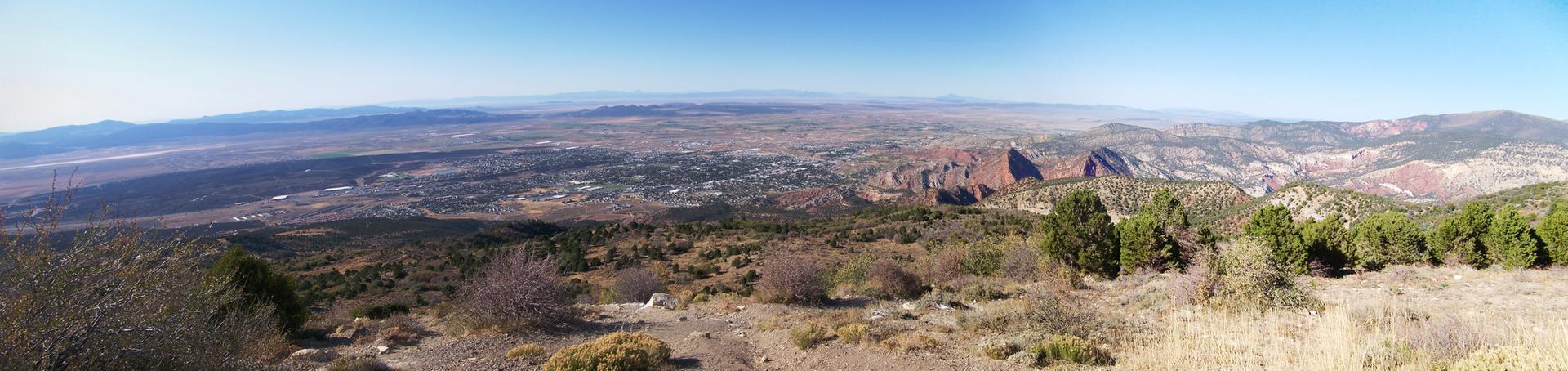 Panoramic view of a wide valley, red rock formations, and distant mountains.