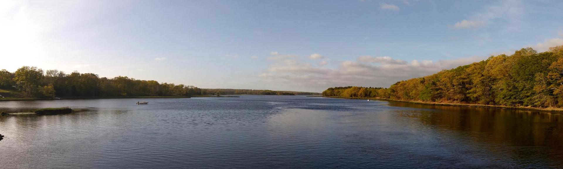 Panoramic view of a wide river bordered by autumn trees under a blue sky.