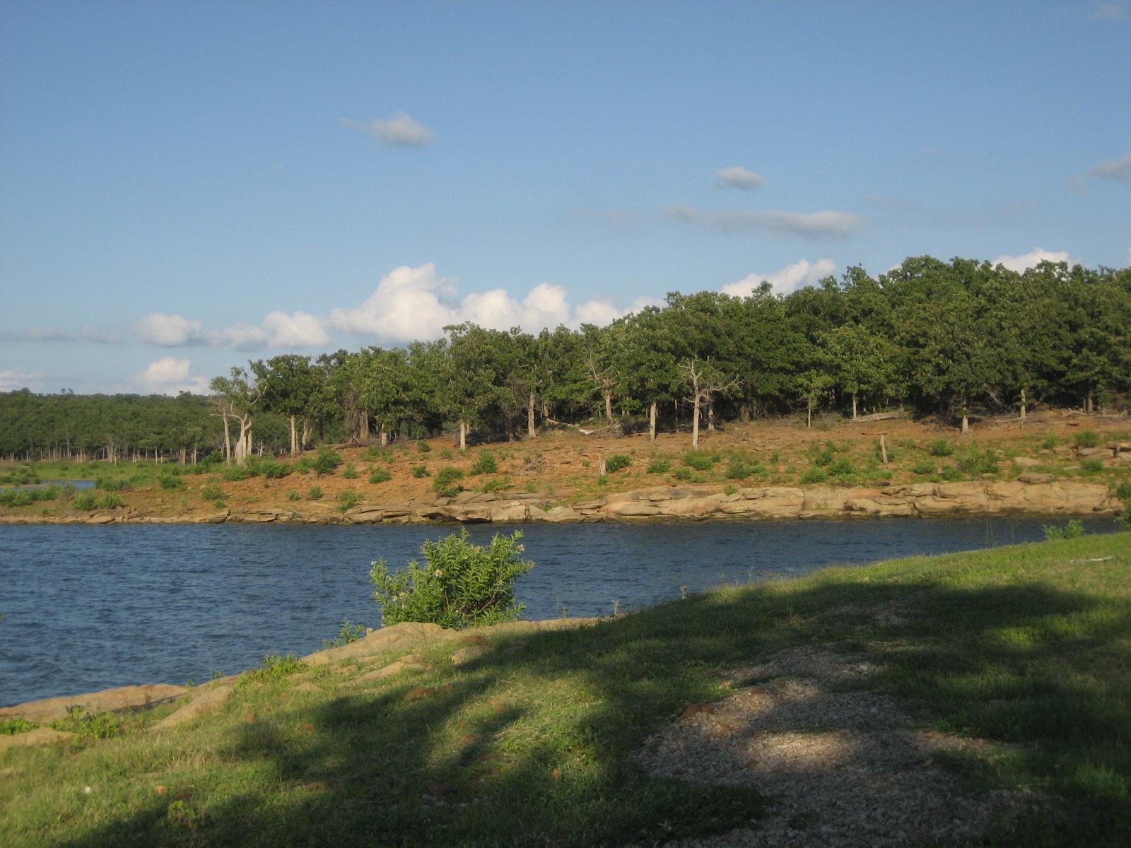 Blue lake with a forested shoreline under a bright, cloudy sky.