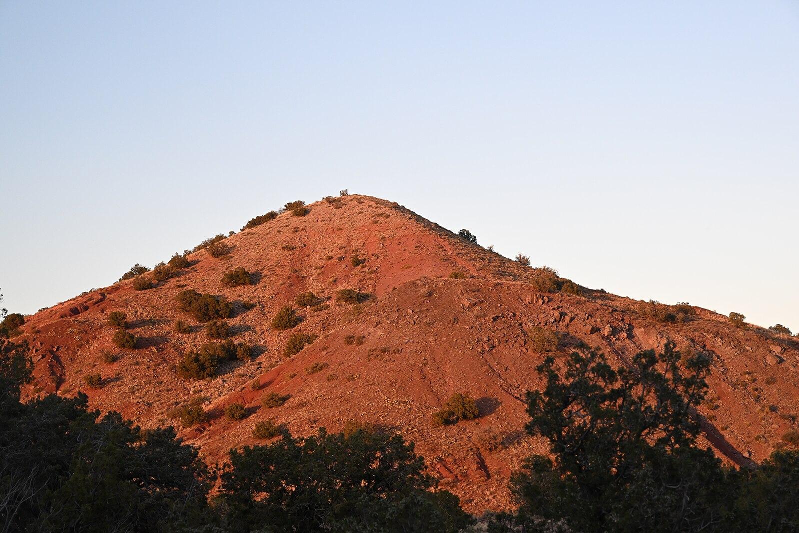 A red-hued hill bathed in warm golden hour light, with dark trees.