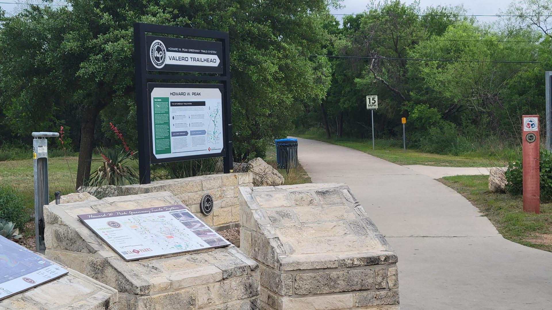 Trailhead sign and information boards next to a paved path on an overcast day.