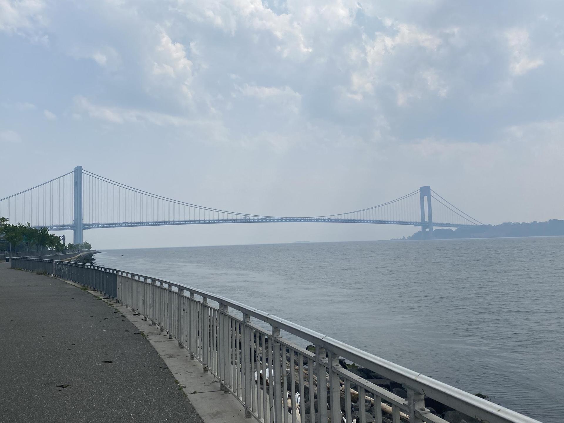Long suspension bridge spanning wide water next to a paved path.