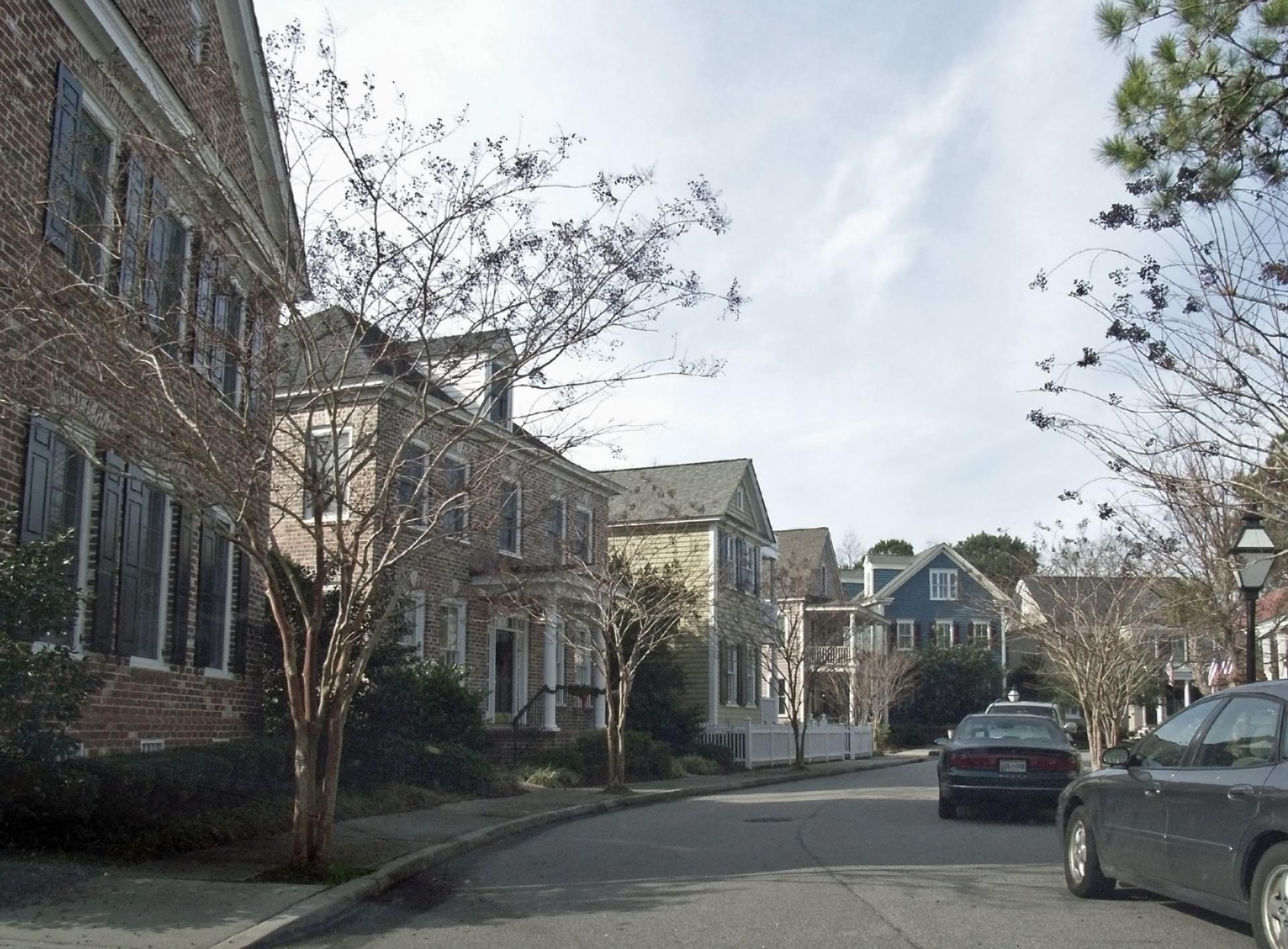 A street with historic houses and bare trees under a bright, cloudy sky.