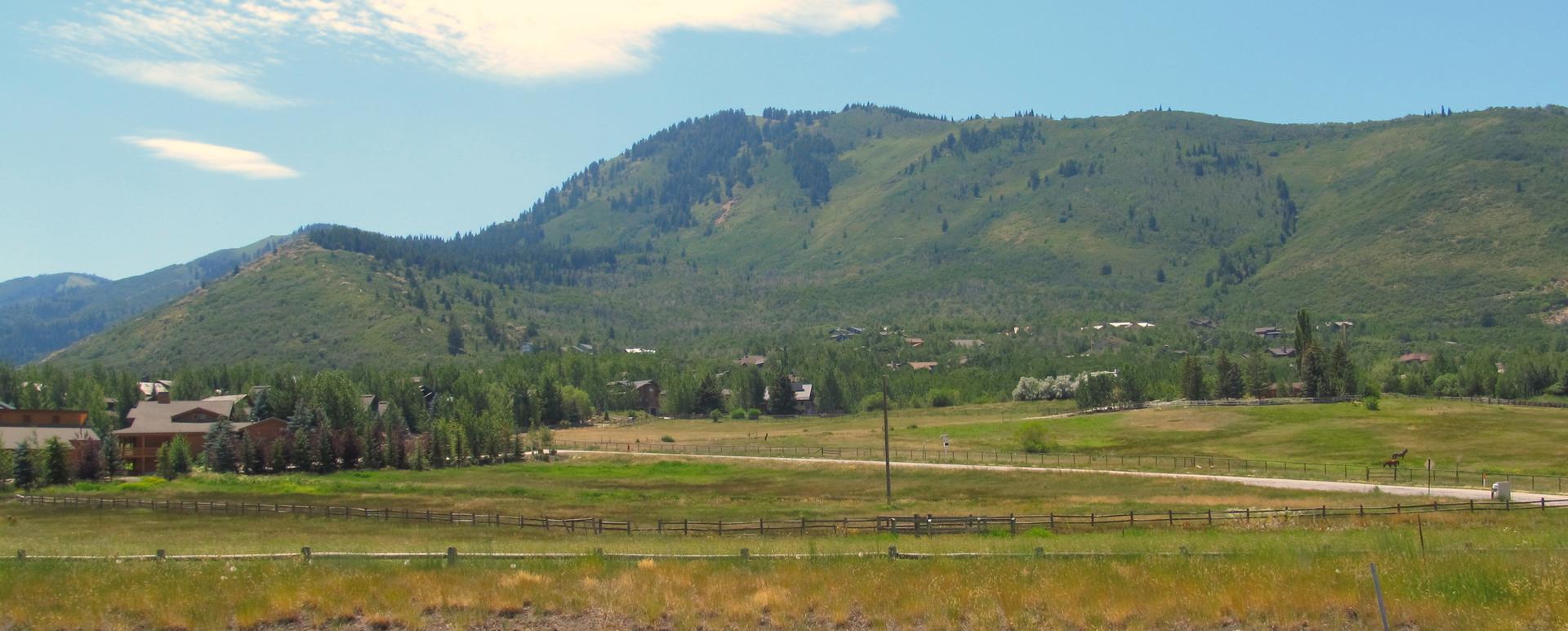 Green mountains rise above fields and scattered houses on a sunny day.