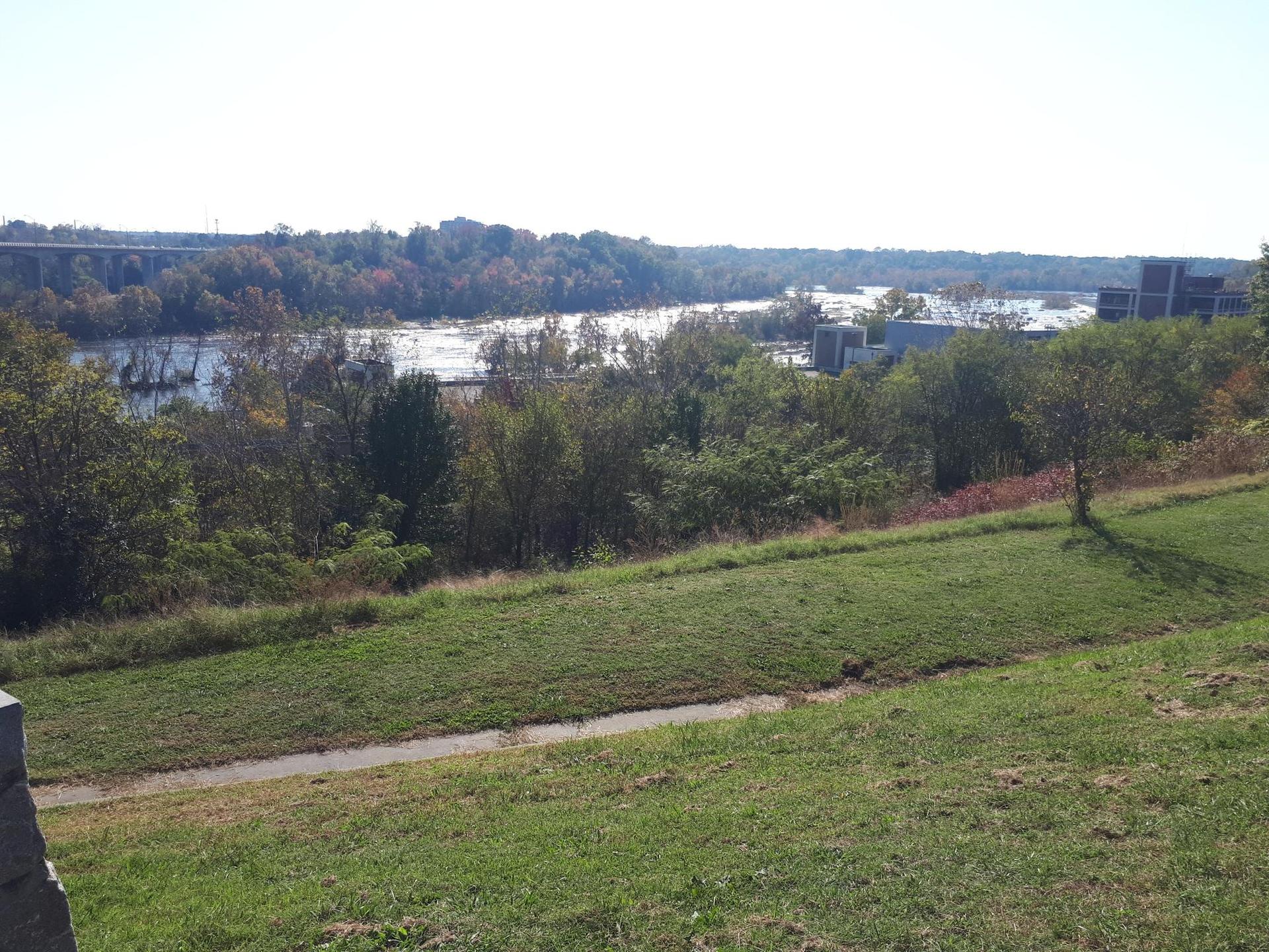 Grassy hill overlooking a wide river with rapids and distant trees.